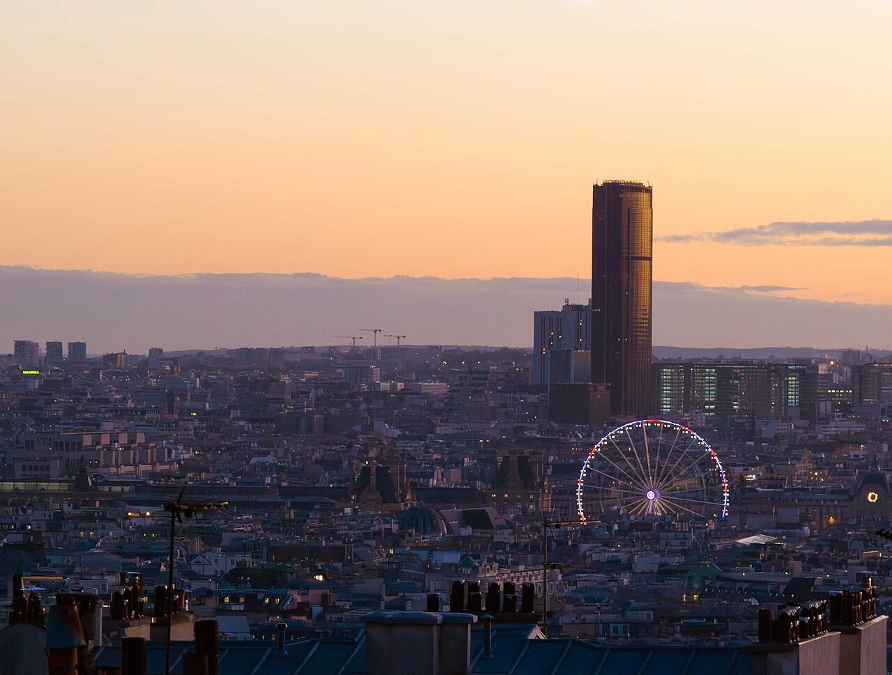 Panorama urbain de Paris au coucher du soleil, avec la tour Montparnasse et la grande roue des Tuileries.
