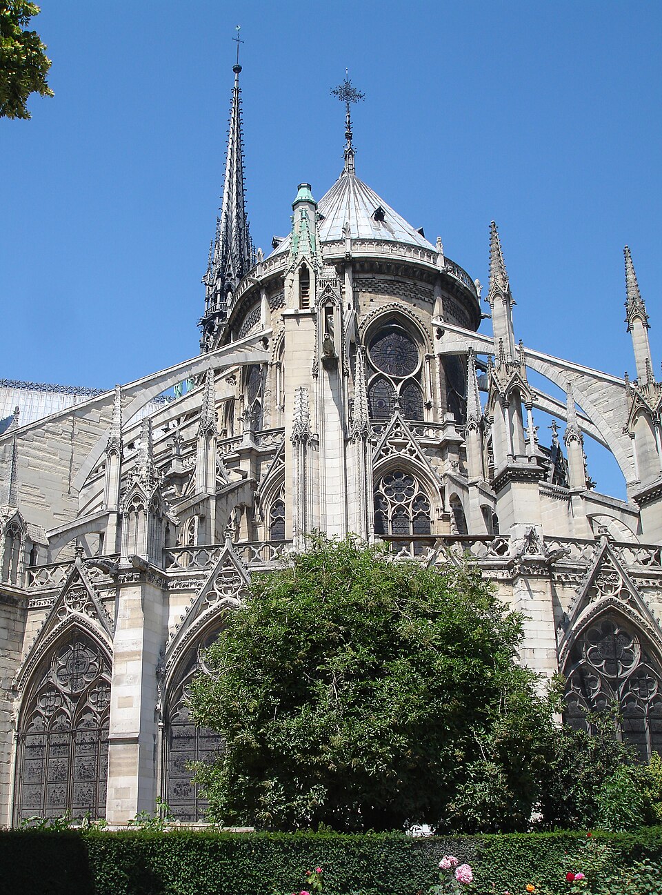 Chevet de Notre-Dame de Paris : de grands arcs relient les murs hauts aux appuis extérieurs ; les baies ont des sommets pointus et des réseaux de pierre. Des arbres masquent une partie basse.